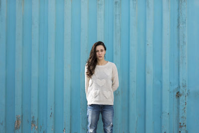 Portrait of woman standing against blue metallic container