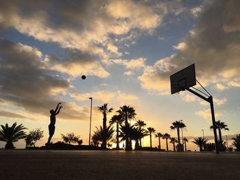 Silhouette man playing basketball on road against sky during sunset