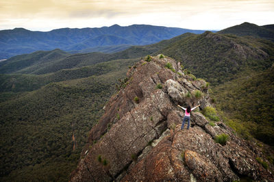 High angle view of woman with arms raised standing on mountain against sky