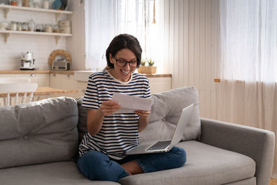 Excited young woman sit on sofa at home receiving job enjoy exam results or college admission letter