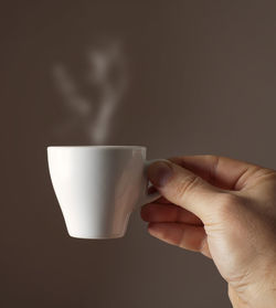 Cropped image of hand holding coffee cup against black background