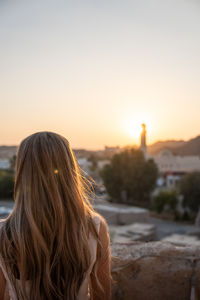 Rear view of woman looking at beach against sky during sunset
