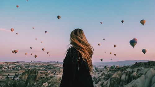 Rear view of woman with hot air balloons against sky during sunset