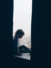 Side view of girl sitting by window at home