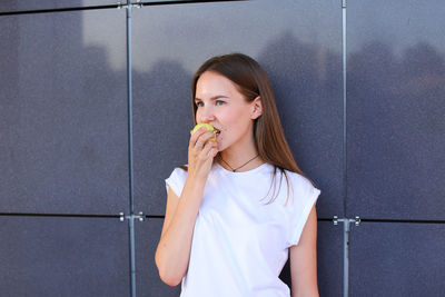 Young woman using mobile phone while standing against wall