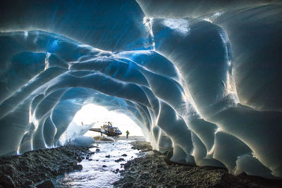 Helicopter parked next to entrance of ice cave during luxury tour.