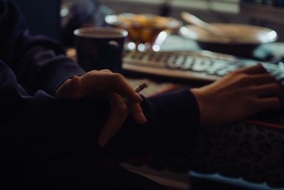 Cropped hands of person holding cigarette while using computer