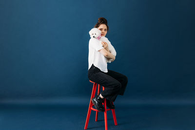 Woman with dog sitting on stool against blue background