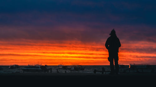 Silhouette man standing on beach against orange sky