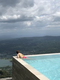 Woman swimming in infinity pool against cloudy sky
