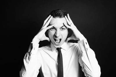 Portrait of businessman screaming against black background