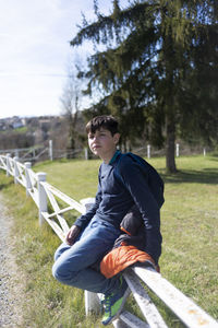 Young teenager male sitting on countryside fence looking camera