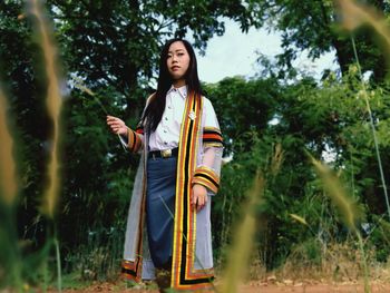 Portrait of young woman standing against trees