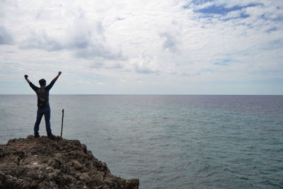 Man standing on rock by sea against sky