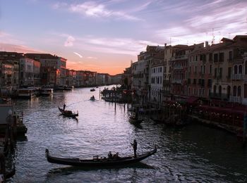 Gondolas on canal in city against sky during sunset