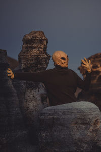 Side view of man sitting on rock against clear sky