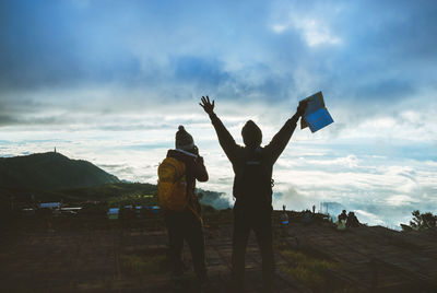 Rear view of people standing on mountain against sky