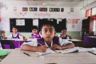 Portrait of boy writing on paper at desk in classroom