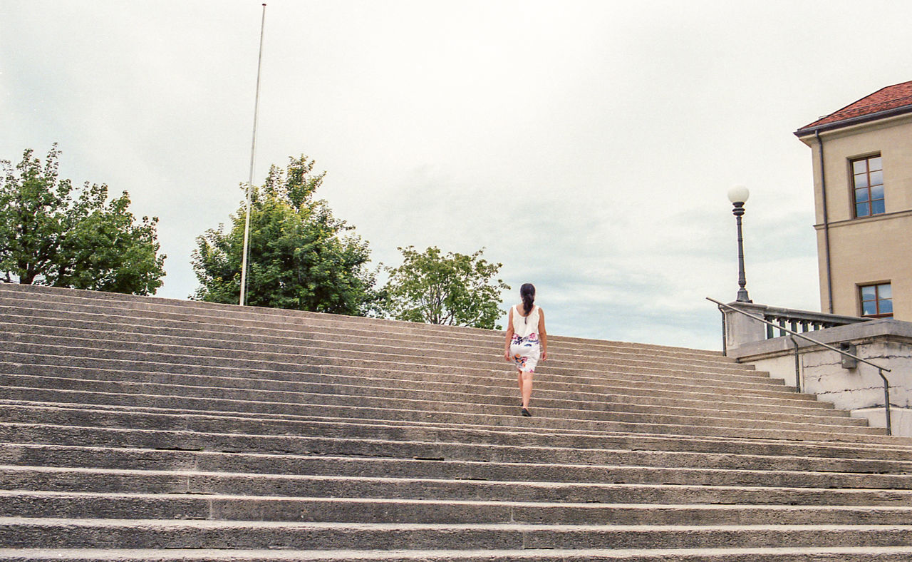 LOW ANGLE VIEW OF WOMAN AGAINST STAIRCASE