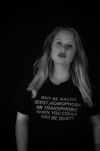 Portrait of young woman wearing t-shirt with text against black background