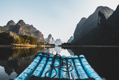 Blue wooden raft in lake with mountains in background against clear sky