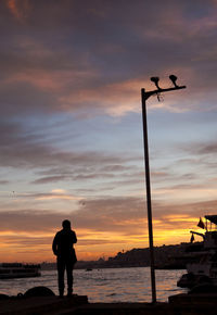 Silhouette man standing on beach against sky during sunset