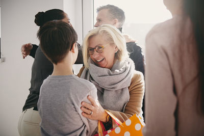 Happy grandmother talking to grandson while senior father embracing daughter at home