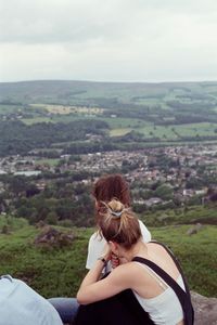 Rear view of woman sitting on landscape against sky