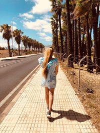 Rear view of woman walking amidst trees against sky