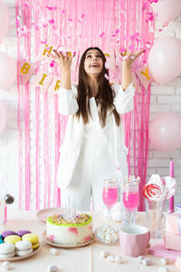  woman preparing birthday table with cakes, cakepops, macarons and other sweets, throwing confetti