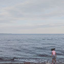 Rear view of girl standing on shore against sky