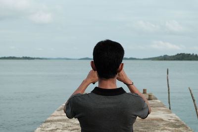 Rear view of man standing on pier by sea against sky