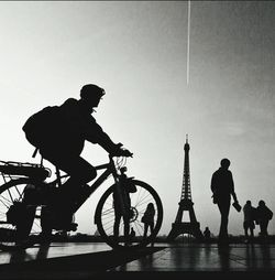 Silhouette people riding bicycle on road against clear sky at dusk