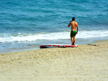 Rear view of man standing by surfboard on beach