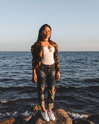 Portrait of young woman standing on rock against sea at beach