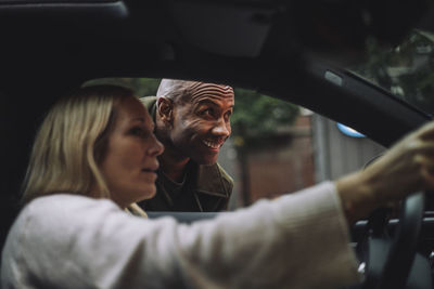Smiling man looking away while talking to woman sitting in car