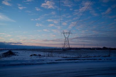 Silhouette electricity pylon on snowcapped field at sunset