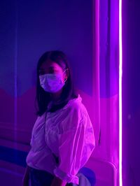 Young woman standing against illuminated wall