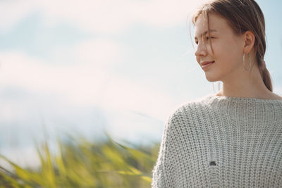 Young woman looking away while standing on field against sky