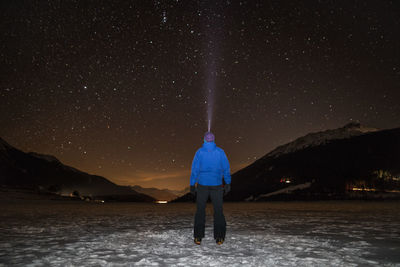 Rear view of hiker standing on frozen lake against starry field at night during winter