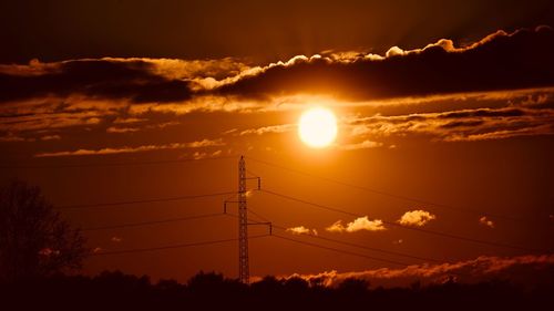 Low angle view of silhouette electricity pylon against sky during sunset