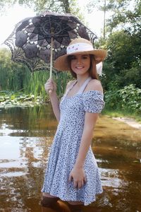Portrait of woman holding umbrella standing against pond