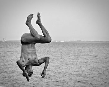 Full length of shirtless man jumping in sea against sky