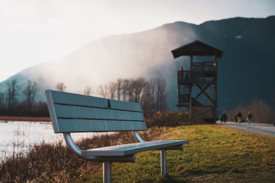 Empty bench on field against sky