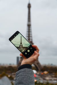 Midsection of person holding smartphone to take from eifel tower in paris