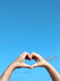 Hand holding heart shape against blue sky