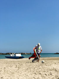 Man on beach against clear sky with football equipment