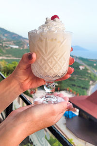 A beautiful wine glass with a pina colada milkshake background of the seashore in women's hands.