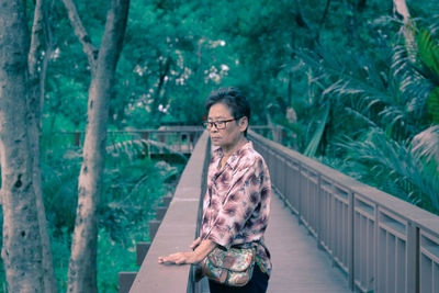 Mature woman standing on footbridge in forest