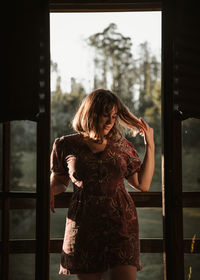 Portrait of young woman standing on ledge of wooden cabin at sunset